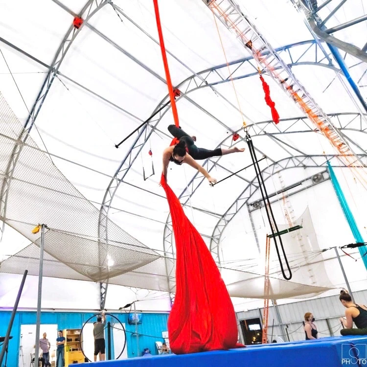 Aerialist suspended in a pose on red aerial silks at Dallas Circus Center