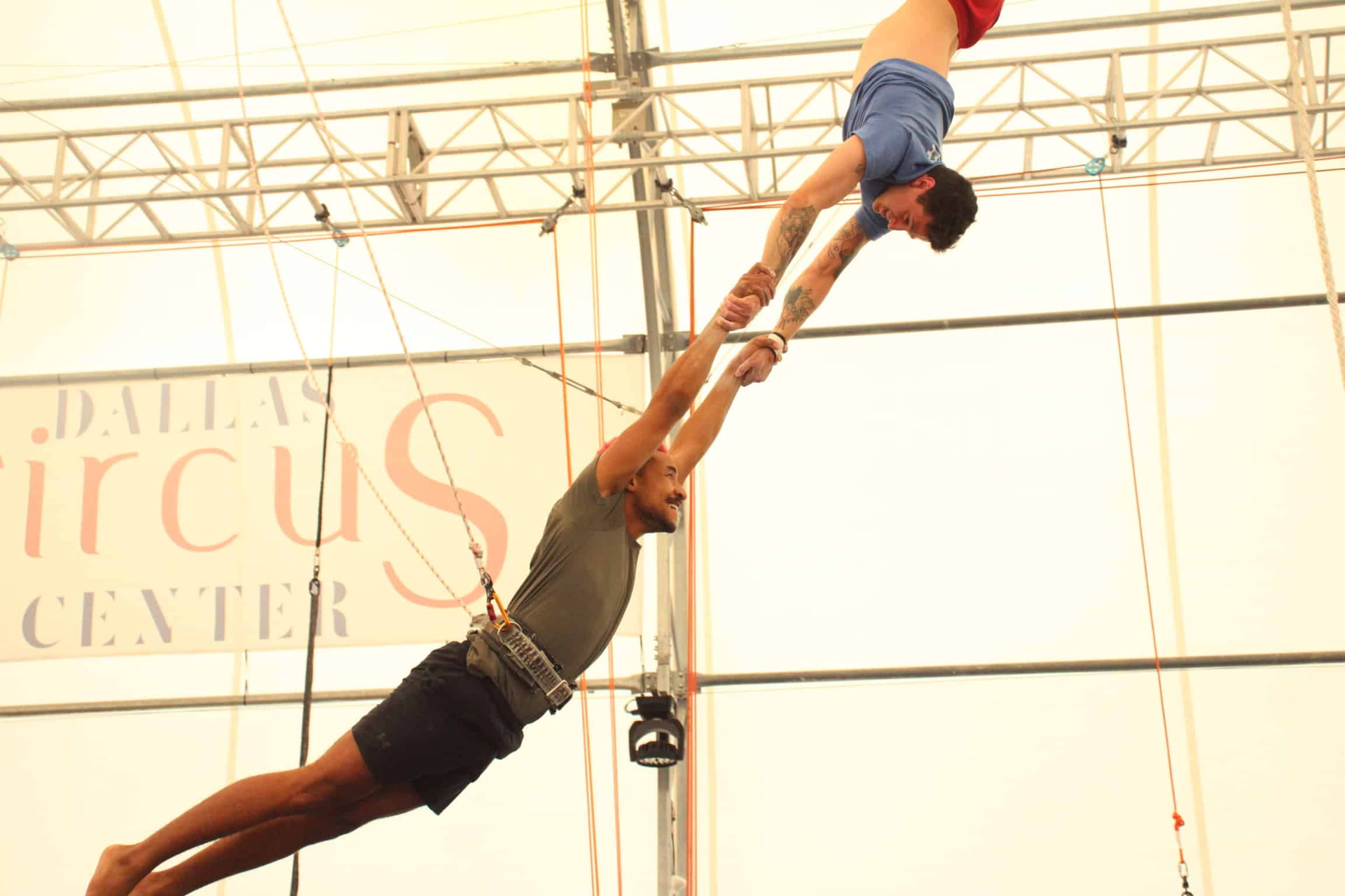Flying trapeze student being caught mid-air by a catcher at Dallas Circus Center